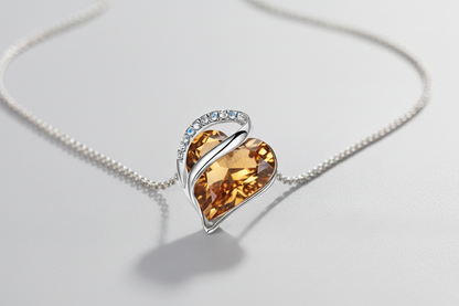 Heart-shaped crystal pendant on a chain against a light gray background